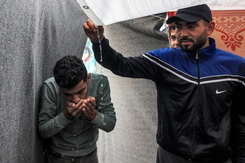 شاب في غزة يشرب الماء من بقايا الأمطار العالقة بالخيمة شاب في غزة يشرب الماء من بقايا الأمطار العالقة بالخيمة
