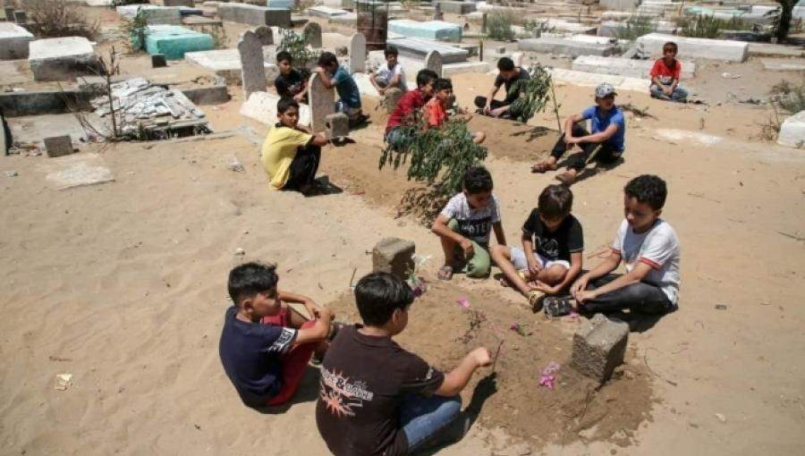 أطفال يجلسون حول قبور الشهداء الخمسة في غزة