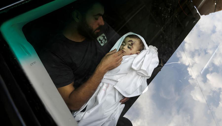 فلسطيني يحمل طفلا استشهد جراء العدوان الإسرائيلي على غزة فلسطيني يحمل طفلا استشهد جراء العدوان الإسرائيلي على غزة