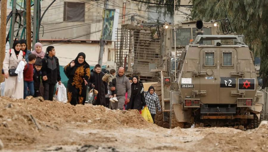 فلسطينيون يسيرون بجوار آليات عسكرية للاحتلال أثناء مغادرتهم مخيم جنين في الضفة الغربية فلسطينيون يسيرون بجوار آليات عسكرية للاحتلال أثناء مغادرتهم مخيم جنين في الضفة الغربية