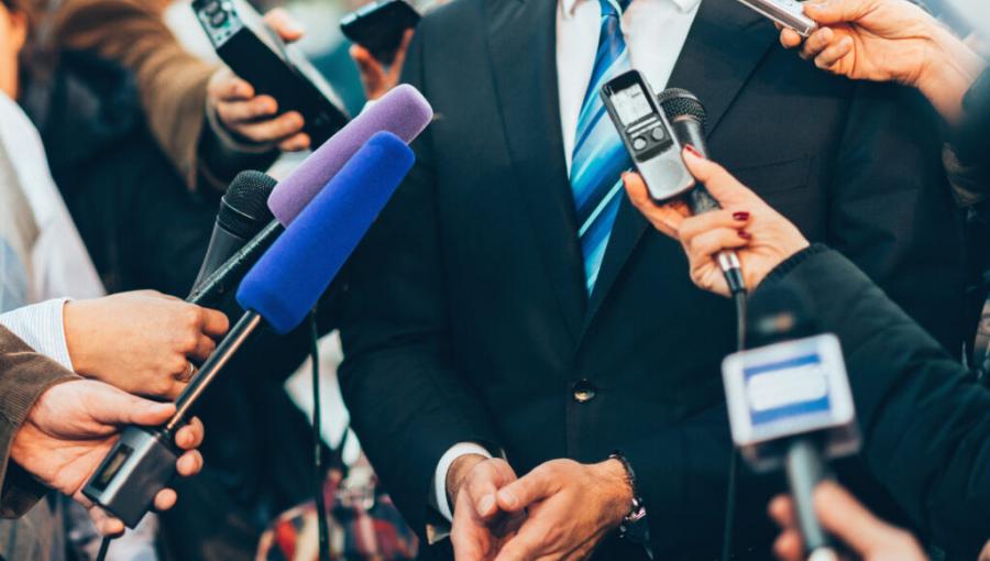 رجل يرتدي بدلة رسمية يحيط به عدد من الصحفيين، تتجه نحوه ميكروفونات وأجهزة تسجيل لتوثيق تصريحاته الصحفية | istockphoto