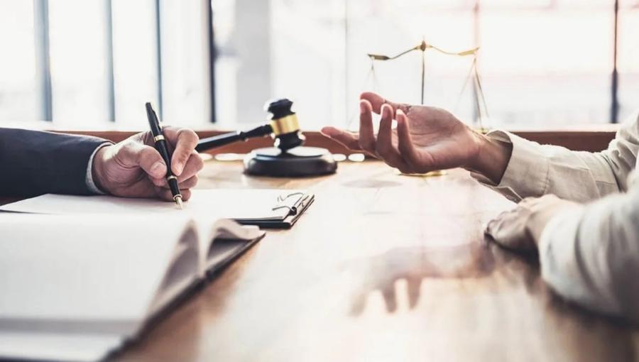 شخصان على طاولة أمام أوراق رسمية مع مطرقة قاض وميزان العدالة في دلالة على المطالبة بالحقوق | تعبيرية