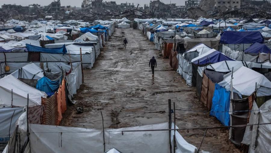 فلسطينيان يسيران  بطريق موحل في مخيم  يؤوي نازحين بعد هطول أمطار غزيرة في حي الزيتون بمدينة غزة | المصدر: وكالة الأنباء الفرنسية