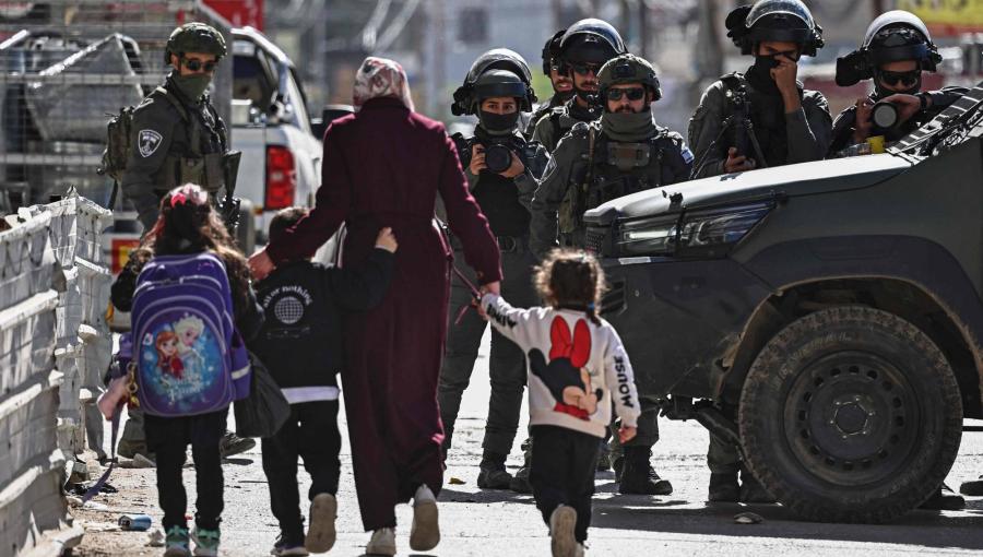 فلسطينية بصحبة أطفال يمرون قرب قوات الاحتلال الإسرائيلية التي اقتحمت حي كفر عقب قرب رام الله في الضفة الغربية 26/1/2026 | وكالة الأنباء الفرنسية