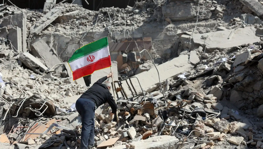 رجل يرفع علم إيران على ركام دمار خلفته غارات الاحتلال الإسرائيلي على إيران | وكالة الأنباء الفرنسية