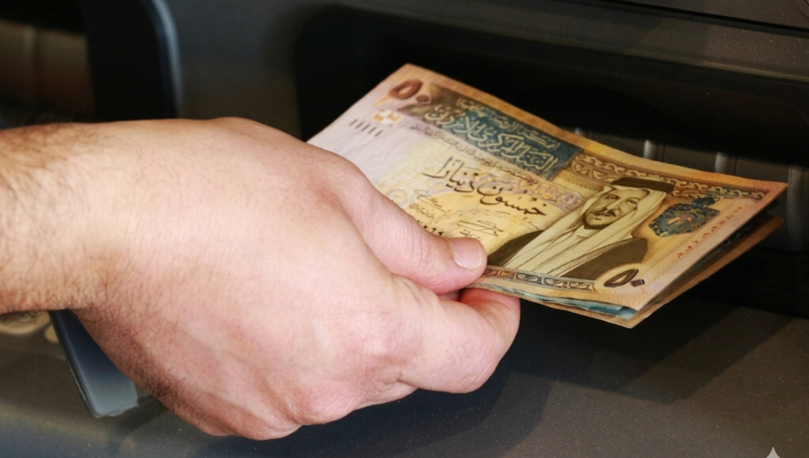 شخص يمسك مبلغا ماليا يخرج من جهاز الصراف الآلي