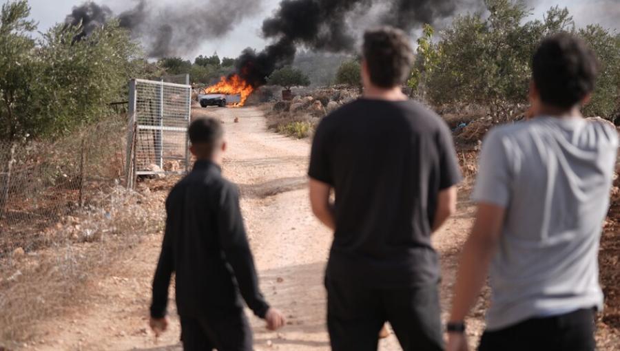 فلسطينيون يقفون بالقرب من مركبة تحترق جراء اعتداء سابق للمستوطنين | الأناضول