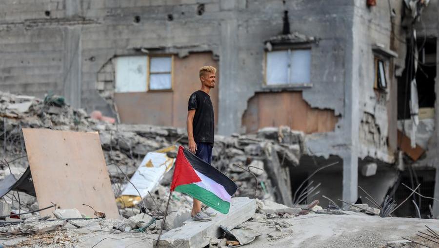 شاب بجانبه العلم الفلسطيني فوق أنقاض مبنى مدمر في جباليا شمالي قطاع غزة 24/10/2025 |شينخوا