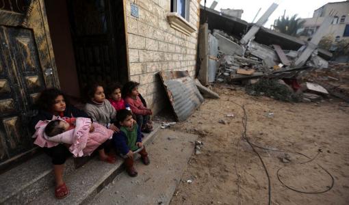 أطفال غزيون يجلسون عند باب بيتهم وحولهم أنقاض جراء قصف الاحتلال