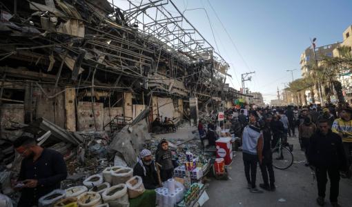 فلسطينيون في غزة في اليوم الأول من شهر رمضان يمشون بجانب باعة قرب المباني المدمرة في مخيم النصيرات للاجئين 11/3/2024 | المصدر: وكالة الأنباء الفرنسية