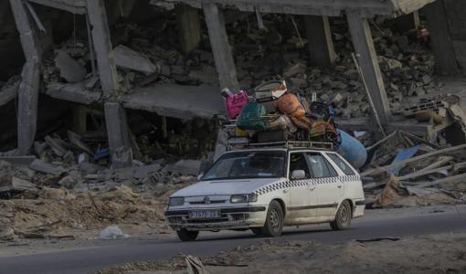 سيارة تقل نازحين فلسطينيين وصلوا إلى خانيونس وخلفهم مبان سكنية قصفها الاحتلال | المصدر: وكالة الأنباء الفرنسية