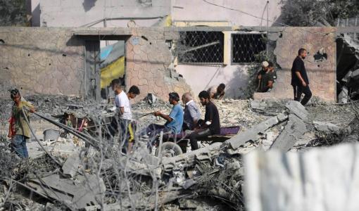 غزيون يمرون بين أنقاض المباني التي دمرها القصف الإسرائيلي في النصيرات | المصدر: وكالة الأنباء الفرنسية