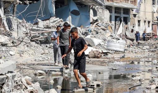 أطفال غزيون يمشون على الطوب لعبور بركة من مياه الصرف الصحي بين الأنقاض على طول شارع في مخيم جباليا | المصدر: وكالة الأنباء الفرنسية