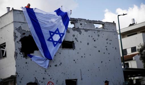 إسرائيليون يعلقون علم الاحتلال الإسرائيلي على مبنى متضرر أصيب بصاروخ من لبنان  في كريات بياليك 22/9/2024 | المصدر: رويترز