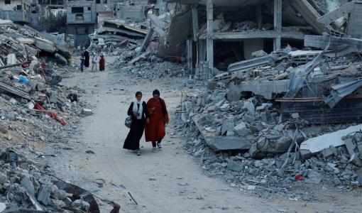 فلسطينيون يسيرون بين أنقاض منازل دمرتها غارات إسرائيلية في خانيونس بقطاع غزة | المصدر: رويترز