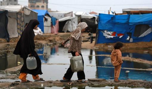 فلسطينيات ينقلن المياه إلى خيمتهن بعد هطول أمطار غزيرة بدير البلح وسط قطاع غزة 24/11/2024 | المصدر: وكالة الأنباء الفرنسية