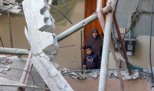 امرأة فلسطينية وطفل يقفان أمام مبنى دمرته غارة إسرائيلية في مخيم النصيرات وسط قطاع غزة | المصدر: وكالة الأنباء الفرنسية