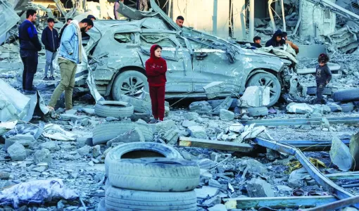 فلسطينيون يقفون أمام سيارة مدمرة وسط أنقاض مبنى منهار بعد قصف إسرائيلي في مدينة غزة 14/1/2025 | المصدر: وكالة الأنباء الفرنسية