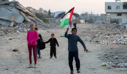 طفل يركض وهو يرفع علم فلسطين في مخيم للنازحين بالبريج وسط قطاع غزة 17/1/2025 | وكالة الأنباء الفرنسية