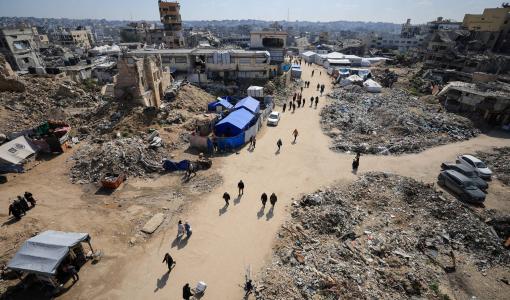 فلسطينيون يسيرون بالقرب من أنقاض المباني في غزة | المصدر: رويترز