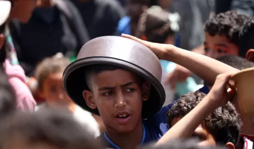 طفل فلسطيني يحمي رأسه من الشمس بوعاء في انتظار الحصول على طعام من تكية في مخيم النصيرات بقطاع غزة طفل فلسطيني يحمي رأسه من الشمس بوعاء في انتظار الحصول على طعام من تكية في مخيم النصيرات بقطاع غزة | المصدر: وكالة الأنباء الفرنسية