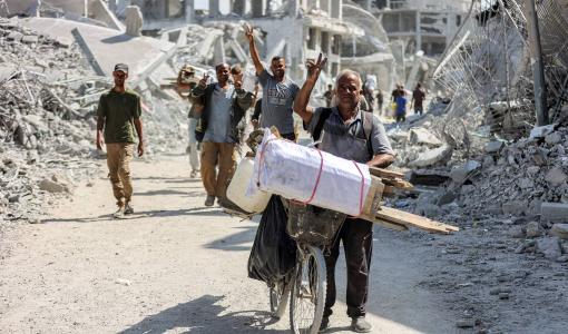 فلسطينيون يسيرون بين مبانٍ مدمرة في وسط خانيونس خلال تحركهم للعودة إلى منازلهم 10/10/2025 | وكالة الأنباء الفرنسية
