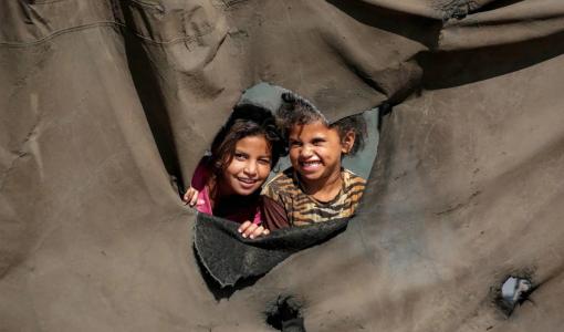 طفلتان تنظران من ثقب في خيمة نازحين بالنصيرات وسط قطاع غزة 7/10/2025 | وكالة الأنباء الفرنسية