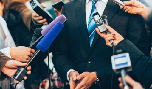 رجل يرتدي بدلة رسمية يحيط به عدد من الصحفيين، تتجه نحوه ميكروفونات وأجهزة تسجيل لتوثيق تصريحاته الصحفية | istockphoto