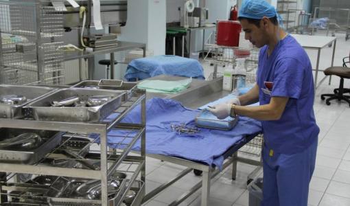 عامل طبي يرتدي لباسا واقيا يقوم بترتيب وتعقيم أدوات جراحية في مستشفى | تعبيرية