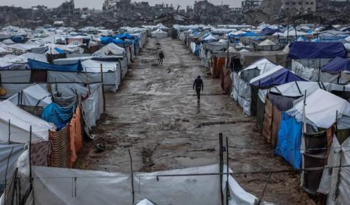 فلسطينيان يسيران  بطريق موحل في مخيم  يؤوي نازحين بعد هطول أمطار غزيرة في حي الزيتون بمدينة غزة | المصدر: وكالة الأنباء الفرنسية