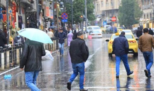 مشهد شتوي من أحد شوارع العاصمة عمان، حيث يسير الناس تحت المطر، بعضهم يحمل مظلات