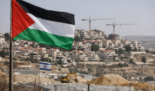 العلم الفلسطيني يرفرف وفي الخلفية مستوطنة إسرائيلية في الضفة الغربية المحتلة