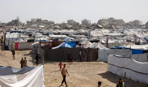 فلسطينيون يسيرون بين مخيمات النازحين المقامة إلى جوار المباني المدمرة في مدينة غزة 16/2/2026 | وكالة الأنباء الفرنسية