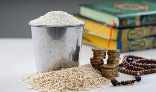 وعاء معدني ممتلئ بحبوب الأرز البيضاء وإلى جانبه نقود معدنية في دلالة على زكاة الفطر