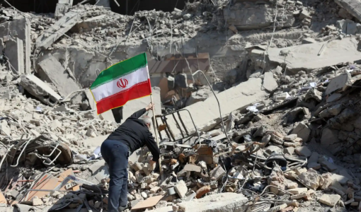 رجل يرفع علم إيران على ركام دمار خلفته غارات الاحتلال الإسرائيلي على إيران | وكالة الأنباء الفرنسية