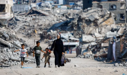 فلسطينيون يسيرون بين أنقاض المباني السكنية التي دمرت خلال العدوان على مدينة غزة | رويترز