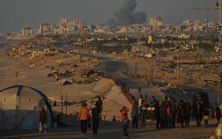 فلسطينيون يسيرون على طول الطريق الساحلي وفي الخلفية دخان يتصاعد إلى السماء بعد غارة شنها الاحتلال على مدينة غزة | أسوشييتد برس