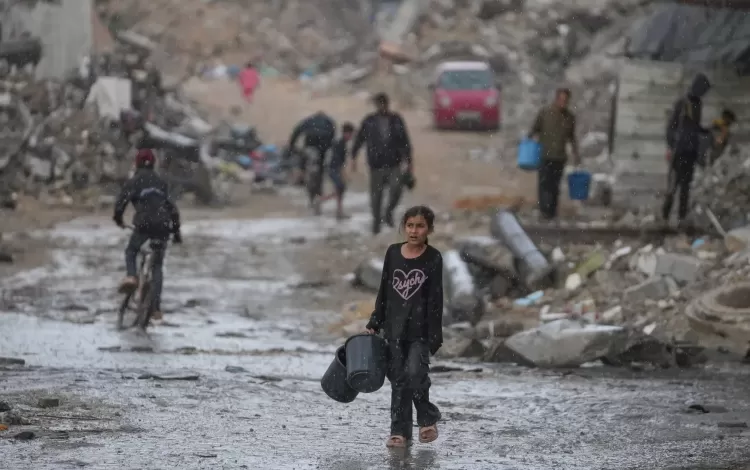 طفلة تحمل دلوين خاليين في طريقها لجلب المياه وسط أمطار غزيرة على حي الشيخ رضوان بمدينة غزة 15/11/2025 | أسوشييتد برس