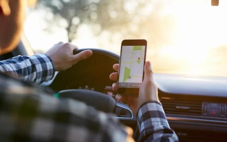 سائق يقود مركبة بينما يمسك هاتفا ويستخدم تطبيقا للنقل | تعبيرية