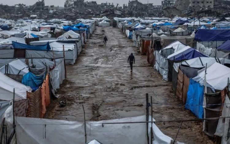 فلسطينيان يسيران  بطريق موحل في مخيم  يؤوي نازحين بعد هطول أمطار غزيرة في حي الزيتون بمدينة غزة | المصدر: وكالة الأنباء الفرنسية