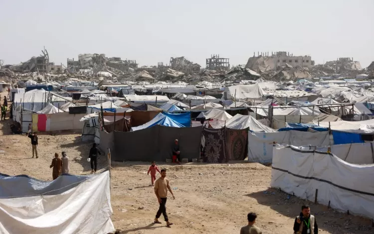 فلسطينيون يسيرون بين مخيمات النازحين المقامة إلى جوار المباني المدمرة في مدينة غزة 16/2/2026 | وكالة الأنباء الفرنسية