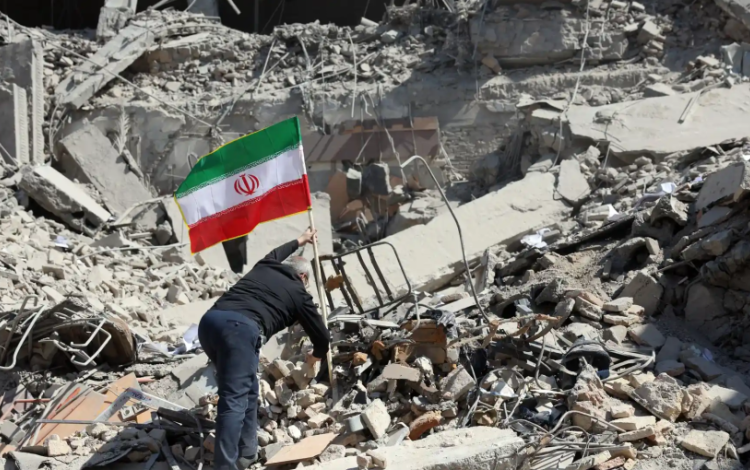 رجل يرفع علم إيران على ركام دمار خلفته غارات الاحتلال الإسرائيلي على إيران | وكالة الأنباء الفرنسية